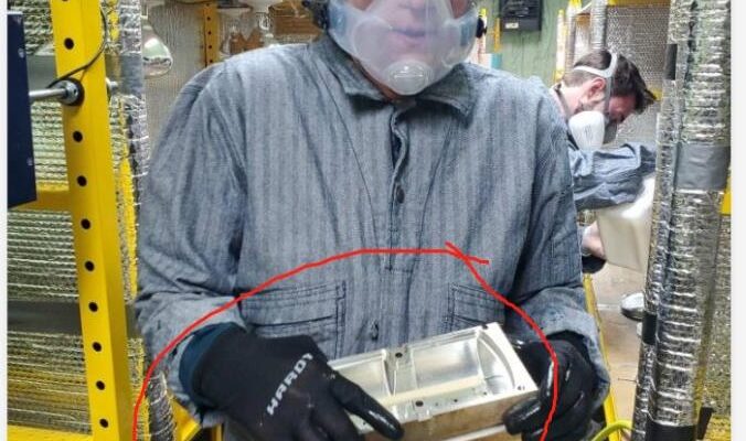 Eileen Durfee wearing a respirator and holding the aluminum mold for a foam roller in the production shop