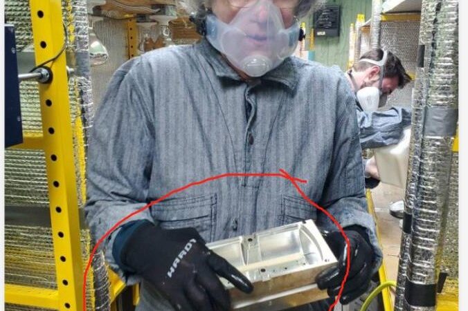Eileen Durfee wearing a respirator and holding the aluminum mold for a foam roller in the production shop
